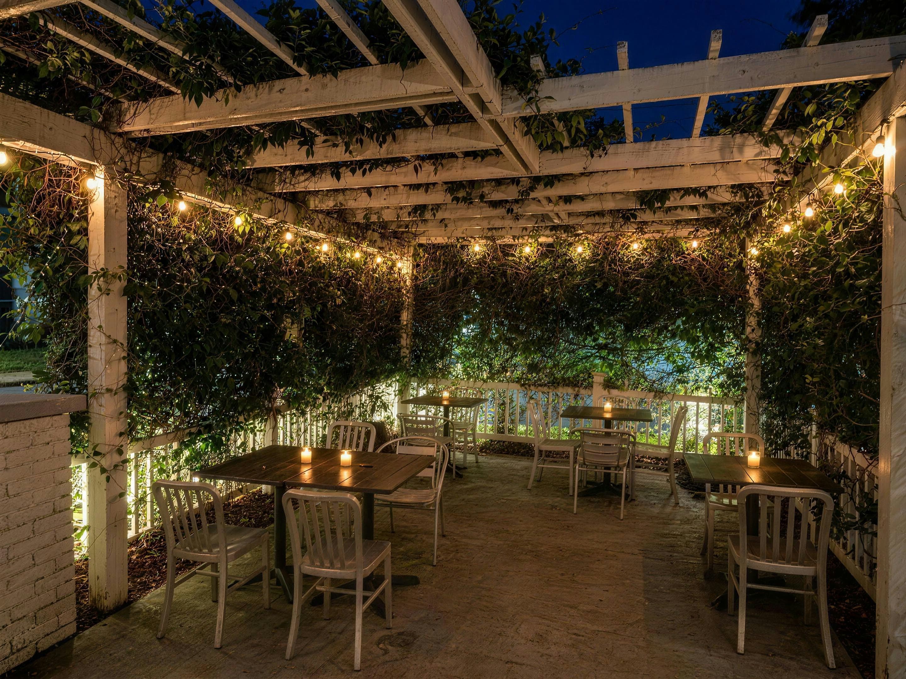The pergola terrasse after dark, string lights and candles glowing over the bistro tables